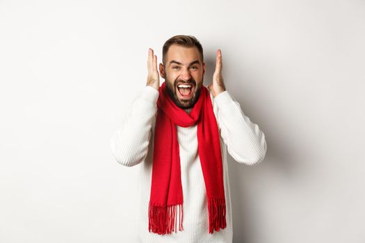 Christmas holidays and New Year concept. Angry man in scream and shout, shaking hands near head with frustrated expression, standing over white background.