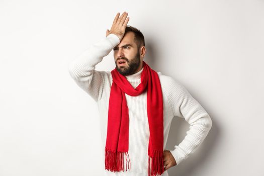 Annoyed man slap his forehead and cursing, forgetting buy christmas gifts, facepalm and standing bothered against white background.