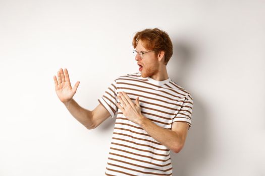 Funny redhead man standing in martial arts pose, fighting shadow and looking left, standing over white background.