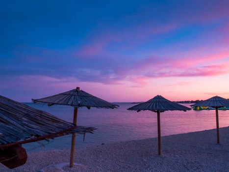 Beach umbrellas, view of the beautiful blue and purple sunset, sky and straw beach umbrellas. Perfect holiday concept. Travel and vacation. Beach on Vir Island, Croatia, Europa. Copy space.