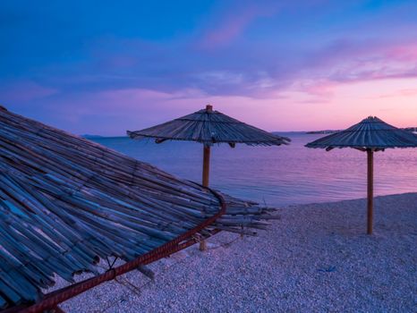 Beach umbrellas, view of the beautiful blue and purple sunset, sky and straw beach umbrellas. Perfect holiday concept. Travel and vacation. Beach on Vir Island, Croatia, Europa. Copy space.