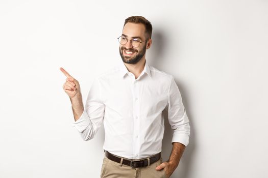 Confident businessman looking satisfied and pointing finger left, showing company banner, standing over white background.