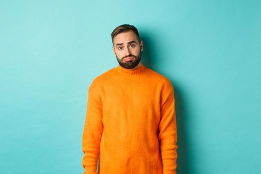 Sad man looking at camera, sulking and feeling distressed, standing over light blue background.