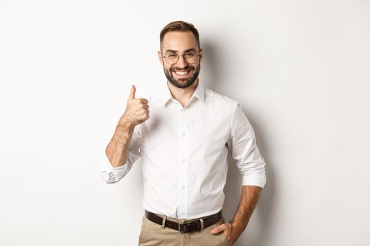 Satisfied successful boss showing thumb up, approve and praise good work, standing over white background.