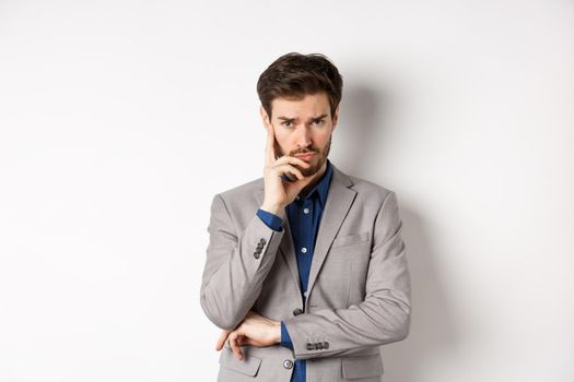 Troubled frowning business man in suit looking at camera pensive, thinking or making decision, standing on white background.