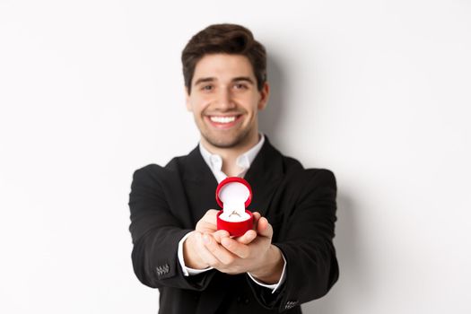 Image of handsome man looking romantic, giving you an engagement ring, making proposal to marry him, standing against white background.