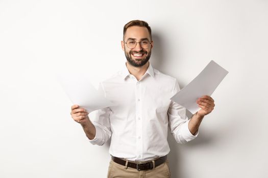 Satisfied boss smiling while holding good report, reading documents, standing over white background.