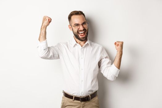 Successful businessman rejoicing, raising hands up and celebrating victory, winning something, standing over white background.