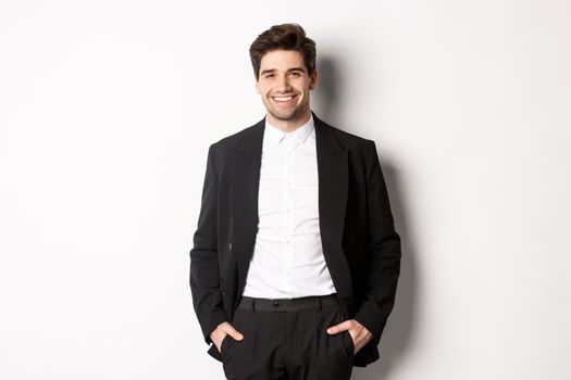 Image of handsome caucasian man in party suit, smiling pleased, attend formal event, standing over white background.