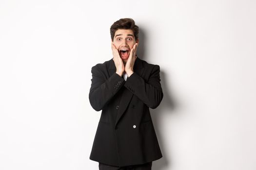 Portrait of surprised handsome businessman in suit, reacting to holidays promo, looking amazed at camera, standing over white background.