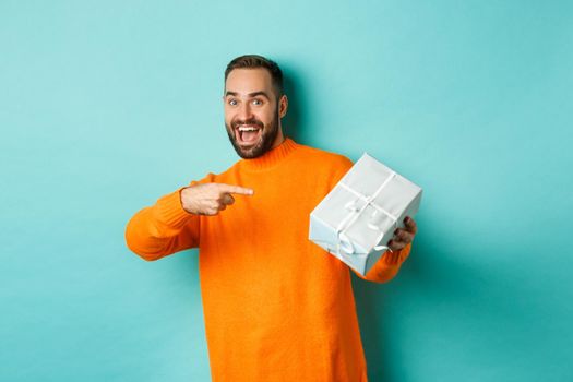 Holidays and celebration concept. Excited man receiving gift, looking happy at present and smiling, standing over blue background.