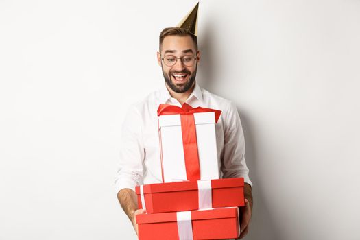 Holidays and celebration. Excited man having birthday party and receiving gifts, looking happy, standing over white background.