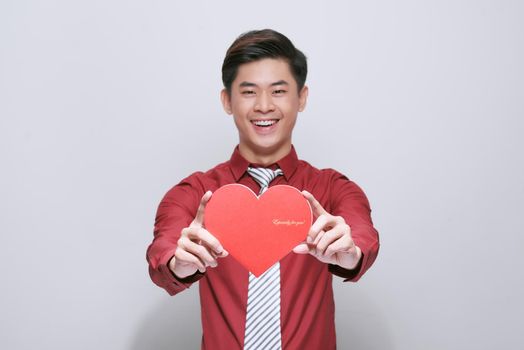 Cute handsome asian holds out a red heart made of paper for Valentine's Day on a white background with copy space