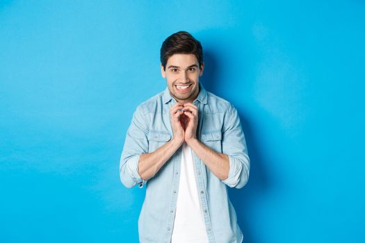 Funny cunning man having evil plan, scheming something and smiling devious, standing against blue background.