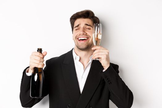 Close-up of handsome drunk guy in suit, holding glass of champagne and celebrating new year, standing over white background.