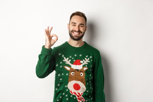 Winter holidays and christmas. Happy bearded man showing okay sign and smiling, approve or agree, praising something good, standing over white background.