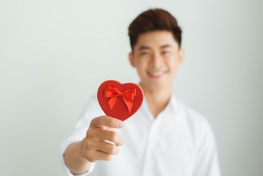 Handsome young man holding red heart box on white background