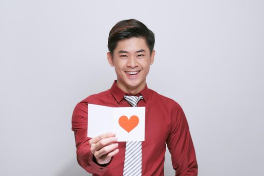 Asian man holding valentines day card with heart, isolated on white