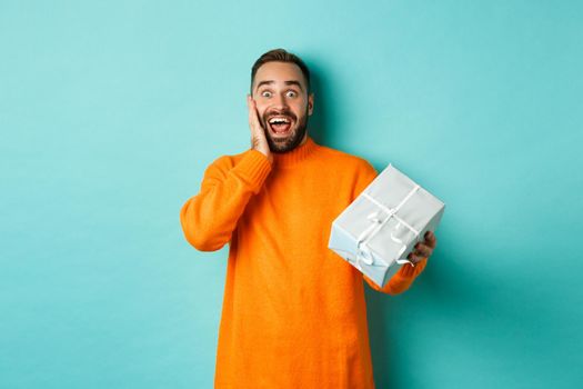 Holidays and celebration concept. Surprised man receiving gift, looking happy at present and smiling, standing over blue background.
