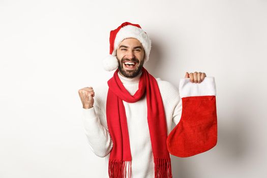 Winter holidays and celebration concept. Happy man holding Christmas sock and rejoicing, receive gift, standing against white background.