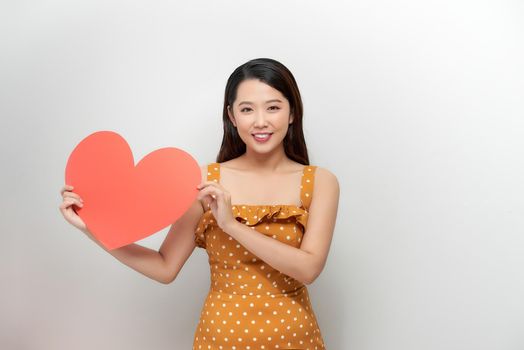 smiling pretty woman looking upwards, holding large red heart to chest daydreaming of men in love,