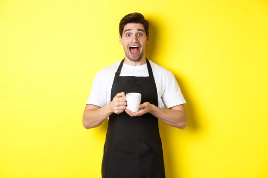 Friendly coffee shop waiter standing with raised hands, place for your sign or logo, standing over yellow background.