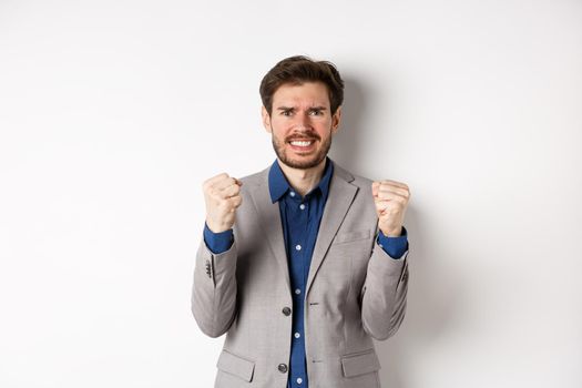 Tensed businessman feeling nervous and pressured, clenching fists and teeth, staring at camera, making money and looking worried, standing on white background.