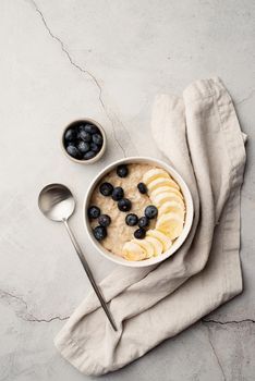 Oatmeal. Porridge with bananas and blueberries for healthy breakfast or lunch. Natural ingredients. Flat lay design on linen napkin and concrete background