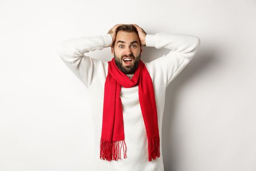 Christmas holidays and New Year concept. Frustrated man holding hands on head, shouting in panic, standing anxious against white background.