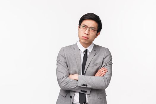 Waist-up portrait of puzzled, serious-looking asian guy in grey suit, looking up frowning and squinting thoughtful, cross hands chest, trying make-up solution, making choice indecisive.