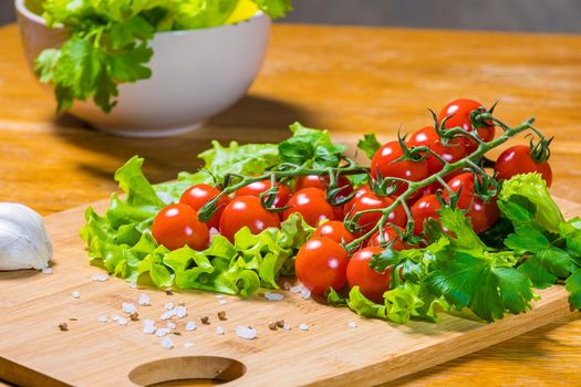 Fresh cherry tomatoes with green salad and garlic on a cutting board. Healthy food concept. Vegetarianism.