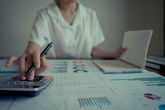 Close up businesswoman hand holding pen using a calculator and reading note book on table office. Statistics and analytic research concept.