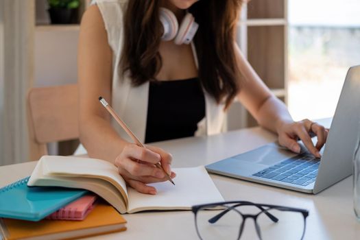 Young business woman sitting at table and taking notes in notebook.On table is laptop, smartphone and cup of coffee.On computer screen graphics and charts. Student learning online