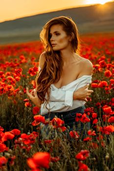 Beautiful young long haired woman in a poppy field at sunset with flying hair. Dressed in a white shirt and denim skirt