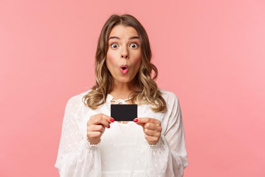 Close-up portrait of excited and amused young girl describe new features of her bank, received new credit card, say wow, folding lips thrilled and amazed, standing pink background.