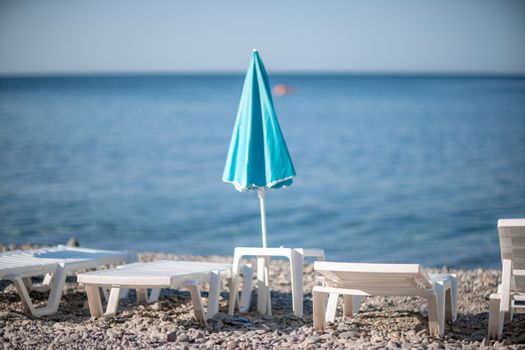 Several white sun loungers and a turquoise parasol on a deserted beach. The perfect vacation concept