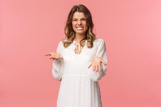 Portrait of dissatisfied, disappointed cute girl in white dress, cringe show tongue, smell something awful, pointing with raised hands at bad unappropriate thing, grimacing dislike, pink background.
