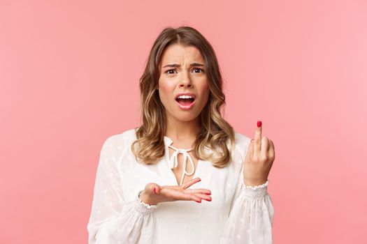 Close-up portrait of frustrated pissed-off, complaining beautiful girl tired of waiting for proposal, pointing at ring finger with bothered grimace, standing pink background disappointed.