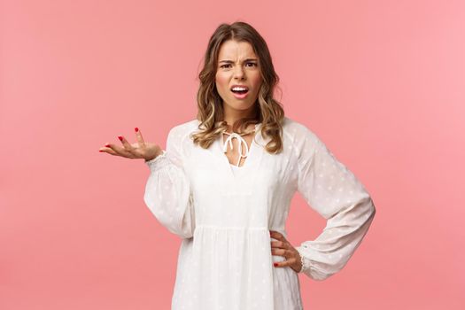 Whats your problem. Pissed-off and annoyed young blond girl looking questioned, cant understand what person complain about, raise on hand in dismay, shrug and grimace puzzled, pink background.