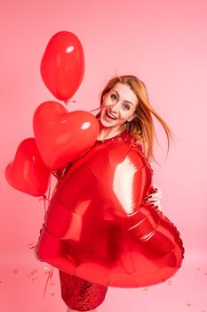 Beautiful redhead girl with red heart baloon posing. Happy Valentine's Day concept. Studio photo of beautiful ginger girl dancing on pink background.