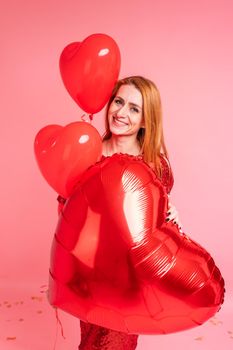 Beautiful redhead girl with red heart baloon posing. Happy Valentine's Day concept. Studio photo of beautiful ginger girl dancing on pink background.