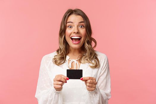 Close-up portrait of excited and happy good-looking blond female recommend bank, smiling amazed, holding credit card, paying for purchase, shopaholic in store feel upbeat.