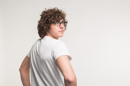 Young man in white t-shirt and glasses turning back at the camera in studio