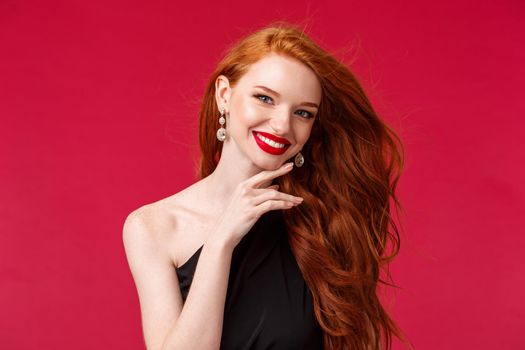 Makeup, beauty and women concept. Close-up portrait of feminine flirty redhead woman, true beauty, touching her jawline gently and smiling, looking camera delighted, red lipstick and black dress.