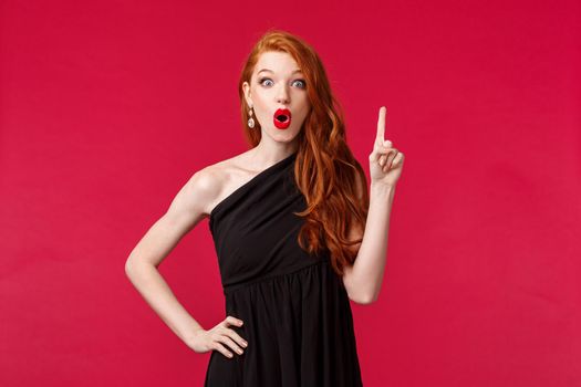 Fashion, luxury and beauty concept. Portrait of creative good-looking redhead woman in luxurious black dress have idea, found solution or way solving problem, raise index finger eureka sign.