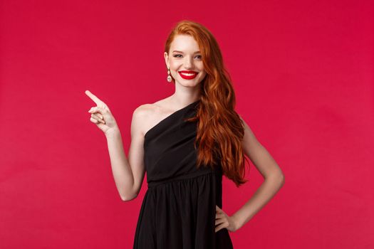 Portrait of cheerful elegant caucasian woman in black dress, evening makeup, attend party or prom, graduate from university, pointing fingers left and smiling, stand red background.