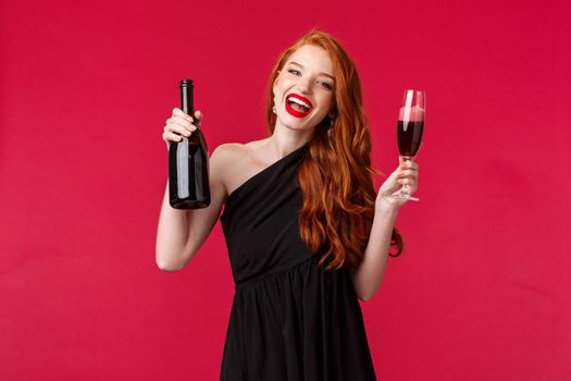 Celebration, holidays and women concept. Festive good-looking young redhead woman drinking at party, enjoying and having fun, hold bottle champagne and glass, smiling camera, wear black dress.