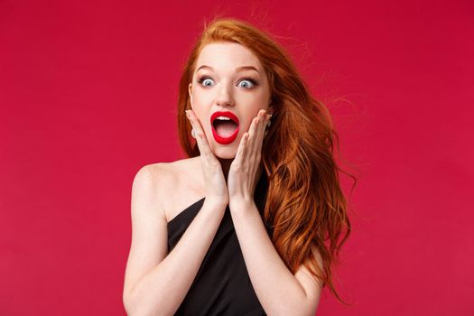 Makeup, beauty and women concept. Close-up portrait of astonished speechless redhead beautiful girl seeing something beautiful and awesome want to have it, losing speech, touch cheeks and drop jaw.