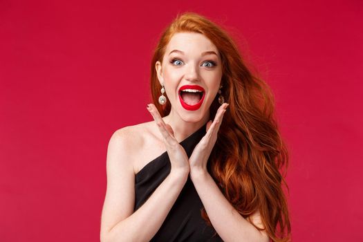 Makeup, beauty and women concept. Close-up portrait of excited beautiful young redhead feminine woman with red lipstick and black dress, clap hands enthusiastic, smiling delighted.