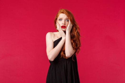 Portrait of insecure and shocked, embarrassed worried redhead woman in makeup and black luxurious dress feel panic of performing in front of people, grab face and look scared camera.
